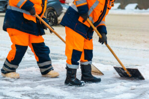 Zwei Personen räumen mit Schneeschaufeln einen verschneiten Weg frei.